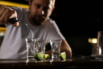 Bartender pouring Mexican Tequila into shot glass at bar counter, closeup. Space for text