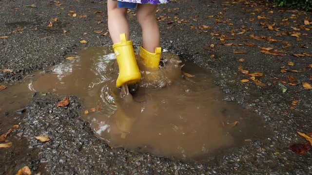 slow motion kid wearing yellow boot playing water rain puddle on road