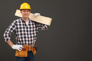Handsome carpenter with wooden planks on dark background. Space for text
