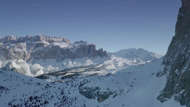 Aerial reveal shot of the ski resort and mountains in Val Gardena in Italian Dolomites. Flying the drone towards the snow capped Sella mountain ridge. Flying by the Saslong mountain on the right.