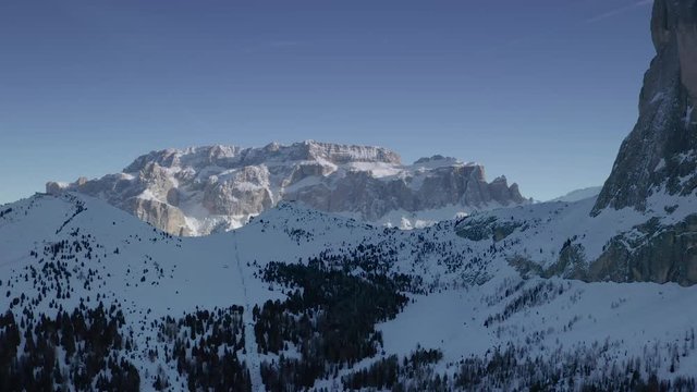 Aerial reveal shot of the ski resort and mountains in Val Gardena in Italian Dolomites. Flying the drone towards the Sella mountain ridge. Saslong mountain is on the right of the frame.