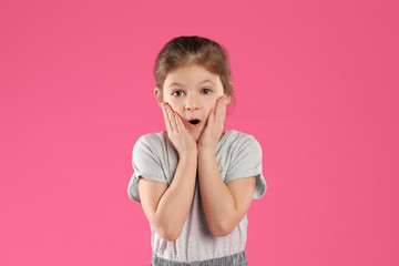 Portrait of shocked little girl on pink background