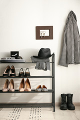 Black shelving unit with shoes and different accessories near white wall in hall
