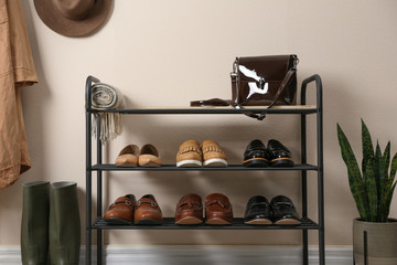 Rack with different shoes near beige wall in room