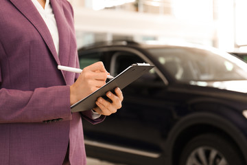 Young saleswoman with clipboard in modern car salon, closeup