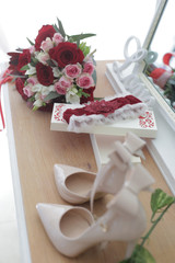wedding accessories on a dressing table: a bride's bouquet of red and pink roses, women's shoes, a garter of the bride