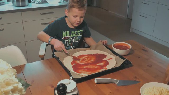 Mutter und Sohn streichen Tomantensauce auf Pizza