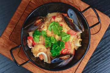 Couscous with seafood in a bowl. Three clams served in a restaurant on wooden cutting board on rustic dark table.