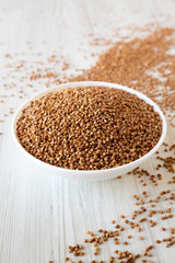 Uncooked Roasted Buckwheat in a white bowl on a white wooden background, low angle view. Close-up.