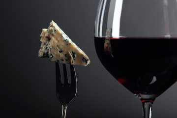 Piece of blue cheese on a fork and red wine.
