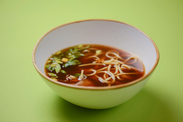 Asian style beef noodles soup served in white bowl over bright green background.