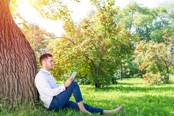 Young man using tablet computer under tree
