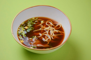 Asian style beef noodles soup served in white bowl over bright green background.