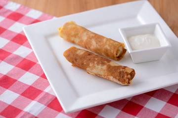 Frech crepes, two savoury pancakes made with flour and milk served with sour cream on a plaid background.