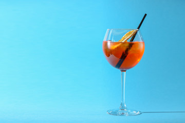 A glass of fruit liqueur in wine glass with a piece of lemon and black plastic straw isolated on pastel blue background.