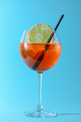 A glass of fruit liqueur in wine glass with a piece of lemon and black plastic straw isolated on pastel blue background.