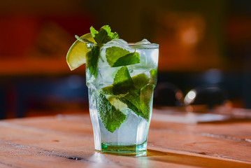 Classic fresh mojito on the table in a bar. Alcohol cocktail with ice, mint and lime on table with blurred background.