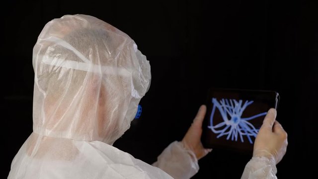 Virologist looking at virus cell on tablet screen. Back view of man wearing protective costume holding tablet and inspecting details of new bacteria. Microbiology concept