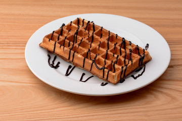Plate of belgian waffles with chocolate caramel sauce on wooden table background. Traditional belgian cuisine, dessert
