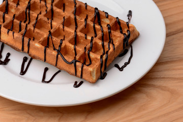 Plate of belgian waffles with chocolate caramel sauce on wooden table background. Traditional belgian cuisine, dessert