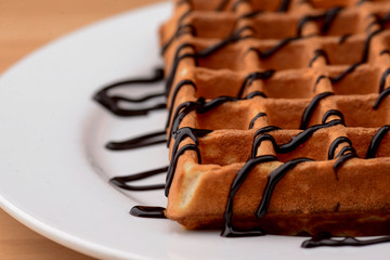 Plate of belgian waffles with chocolate caramel sauce on wooden table background. Traditional belgian cuisine, dessert
