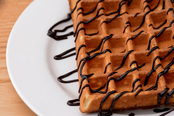 Plate of belgian waffles with chocolate caramel sauce on wooden table background. Traditional belgian cuisine, dessert