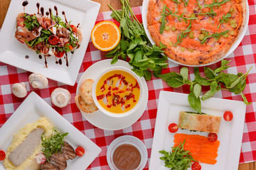 Flat lay shot of delicious italian cuisine. Delicious pizza, salmon rolls, pumplin soup and salad on a wooden table.