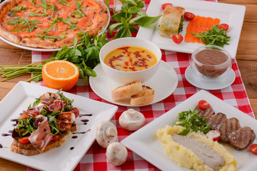 Flat lay shot of delicious italian cuisine. Delicious pizza, salmon rolls, pumplin soup and salad on a wooden table.