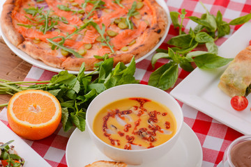 Flat lay shot of delicious italian cuisine. Delicious pizza, salmon rolls, pumplin soup and salad on a wooden table.