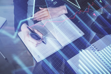 Forex chart hologram on hand taking notes background. Concept of analysis. Multi exposure