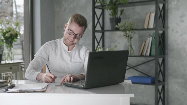 young male entrepreneur working at laptop computer while sitting at table in office, joyful at a job well done raise his hands up background of fresh flowers, concept of success