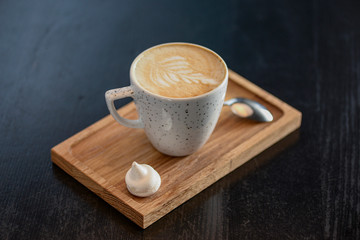 Cup of coffee on the little board over black background. Latte art. Little coffee mug and spoon.