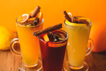 Three glasses of hot red mulled wine with fruit and spices on wooden table on colorful orange...