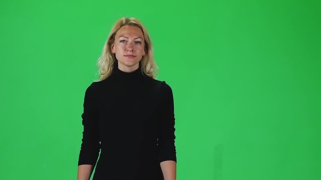 Blonde girl in a black dress going and looking straight into the camera against a green screen. Slow motion