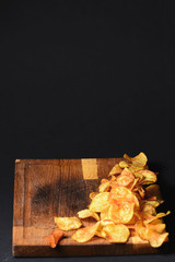 Potato chips served on a wooden cutting board on a black background. American cuisine, food photography, copy space