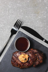 Grilled beef steak medium rare with sauce on black wooden cutting board with utensils. Copy space, flat lay.