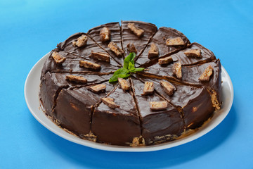 Salted caramel chocolate cake with nuts and vanilla decorated with chocolate pieces and mint leaf on blue background