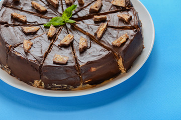 Salted caramel chocolate cake with nuts and vanilla decorated with chocolate pieces and mint leaf on blue background