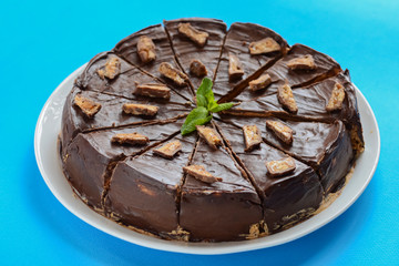 Salted caramel chocolate cake with nuts and vanilla decorated with chocolate pieces and mint leaf on blue background