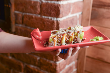 A waiter holds a plate of tasty food with sushi rolls. Japanese cuisine in restaurant