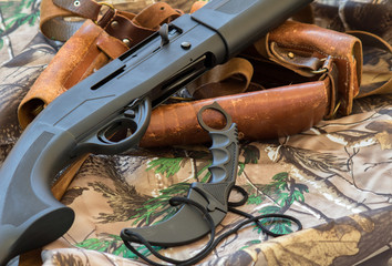 close-up view of black hunting shotgun and karambit knife on the camouflage background