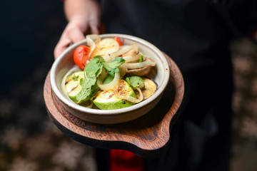 Waiter holds a plate with grilled zucchinis and eggplant on cutting boards in a restaurant.