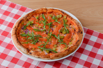 Delicious Italian pizza with salmon fish served on white plate on rustic wooden table with plaid tablecloth.