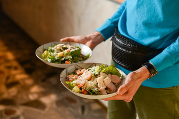 Waiter holds two plates with Italian salad with jamon, prosciutto, fresh vegetables and parmesan cheesein a restaurant