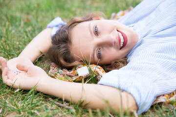 Smiling woman lying on ground in park and looking at camera. Beautiful lady relaxing outdoors. Leisure, relaxation concept