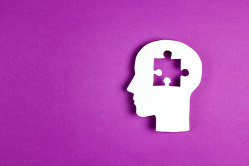 Human head paper silhouette with a puzzle piece cut out on the purple background. Mental health...