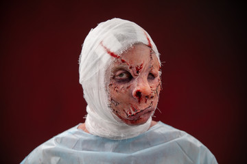 Crazy zombie horror make up. Person in blue madical shirt and bandaged head. Scars, deep scratches...