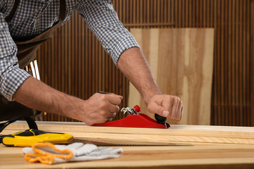 Carpenter working with timber at table indoors, closeup