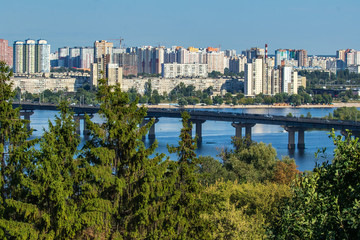 View of the Dnieper, the Paton Bridge and the Left Bank of Kyiv on a sunny day. Skyline of Kyiv. Nature and cityscape together in ukrainian capital. Ukraine.