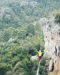 Naklejka premium A man is walking along a stretched sling. Highline in the mountains. Man catches balance. Performance of a tightrope walker in nature. Highliner on the background of valley.